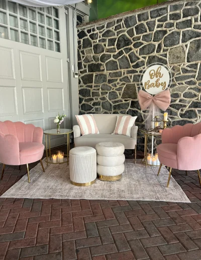 Baby shower lounge setup at Rockwood Carriage House with pink chairs, sofa, candles, and stone wall backdrop