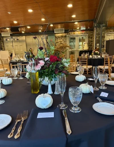Fall wedding reception table setting at Rockwood Carriage House with black linens, white pumpkins, floral centerpiece, and stone wall backdrop