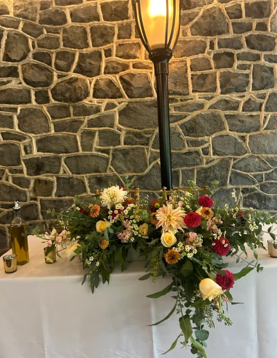 Floral wedding table arrangement at Rockwood Carriage House with colorful flowers, stone wall backdrop, and warm lantern lighting