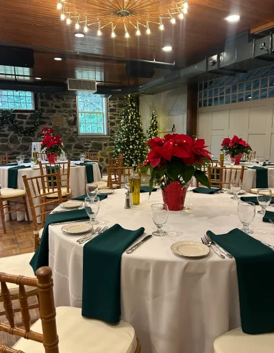 Holiday reception setup at Rockwood Carriage House with poinsettia centerpieces, Christmas trees, stone walls, and green table accents