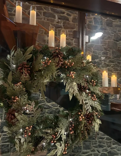 Holiday wreath with greenery, pinecones, copper accents, and candlelight inside Rockwood Carriage House