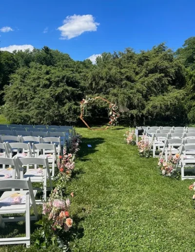 Outdoor wedding ceremony aisle at Rockwood Carriage House with white chairs, floral arrangements, and a garden arch