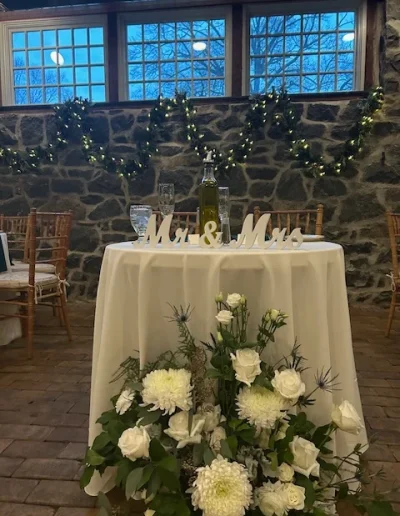 Sweetheart table at Rockwood Carriage House with Mr. and Mrs. sign, white floral arrangement, garland, and stone wall backdrop