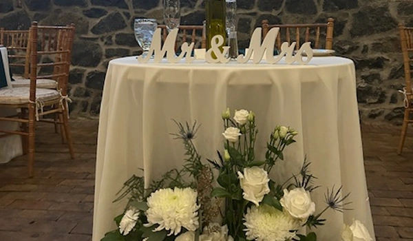 Sweetheart table at Rockwood Carriage House with Mr. and Mrs. sign, white floral arrangement, garland, and stone wall backdrop