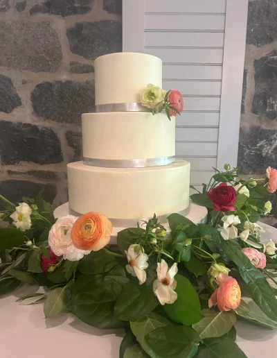 Three-tier wedding cake with silver ribbon and fresh flowers at Rockwood Carriage House