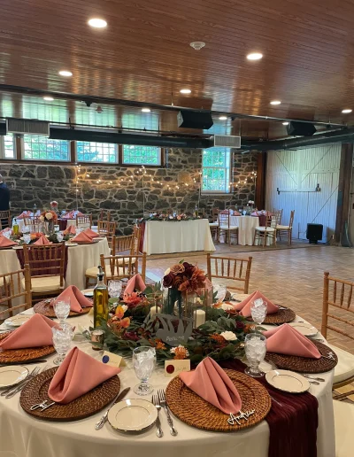 Wedding reception setup at Rockwood Carriage House with pink napkins, burgundy table runner, floral centerpieces, and stone wall backdrop