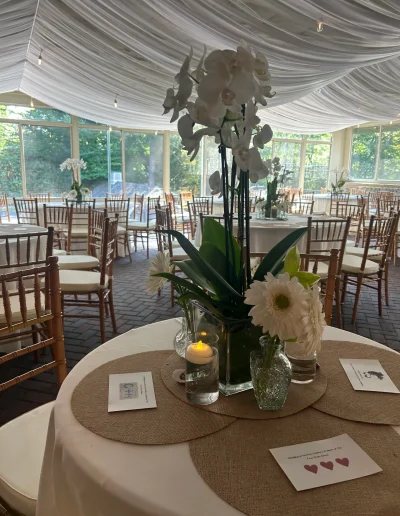 Wedding reception table centerpiece with white orchids, daisies, candles, and draped ceiling at Rockwood Carriage House