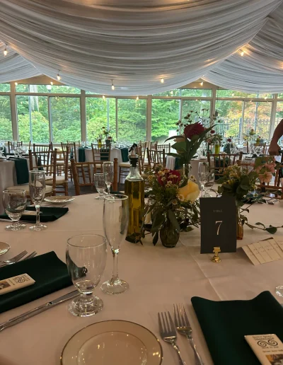 Wedding reception table setting at Rockwood Carriage House with green napkins, floral centerpiece, table number, and draped ceiling