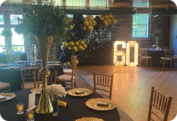 60th birthday celebration setup at Rockwood Carriage House with gold balloons, black linens, and illuminated number display