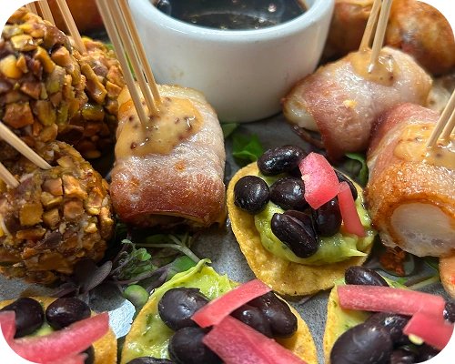 Assorted passed appetizers with bacon-wrapped bites, avocado black bean crostini, pistachio-crusted bites, and dipping sauce