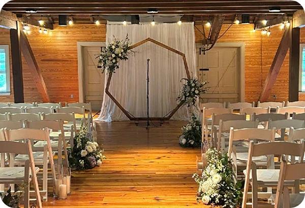 Indoor wedding ceremony setup at Rockwood Carriage House with white chairs, floral aisle arrangements, and hexagon arch