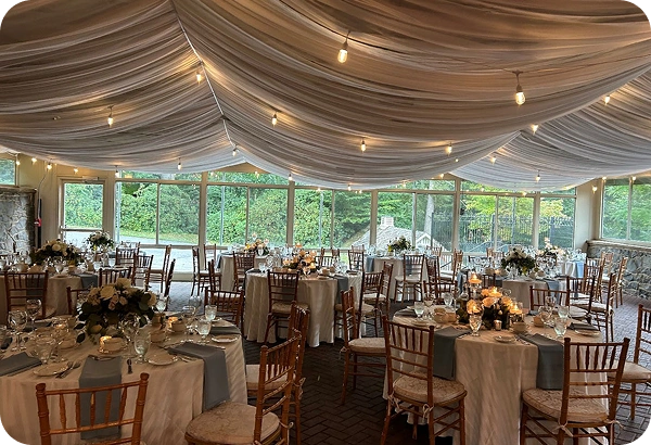 Wedding reception space at Rockwood Carriage House with draped ceiling, string lights, round tables, and garden views