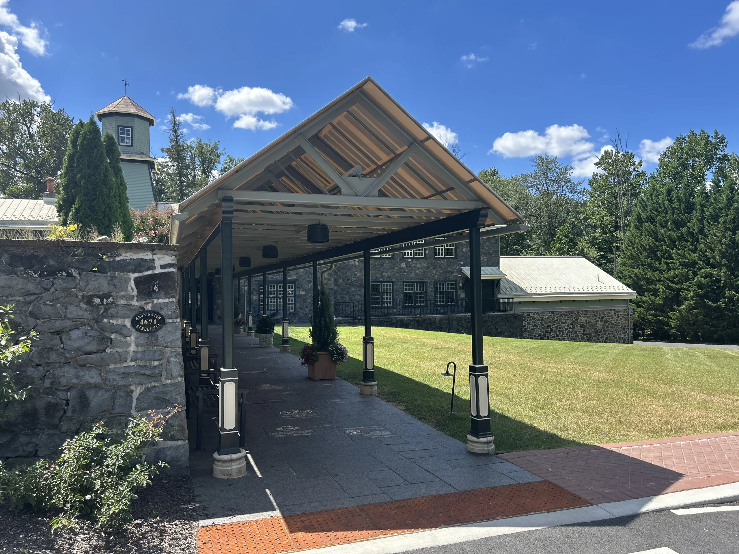 Covered entrance to Rockwood Carriage House with historic stone buildings, cupola, lawn, and address plaque