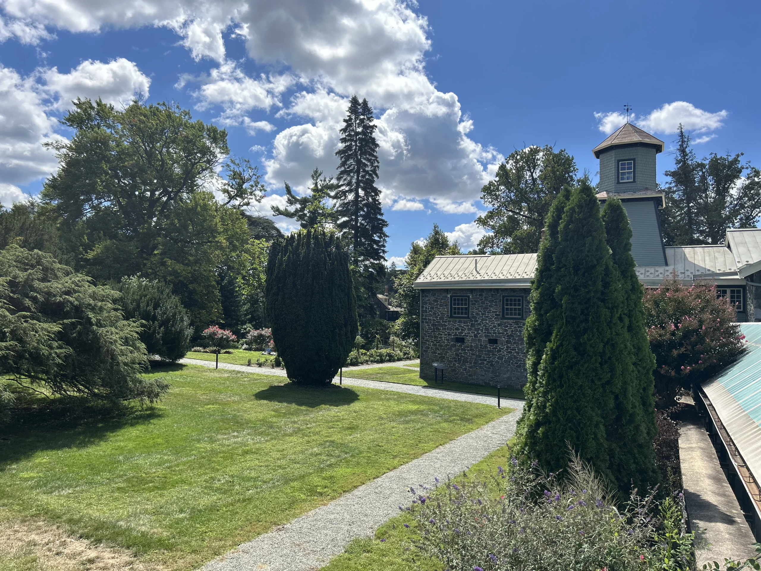Garden pathway beside Rockwood Carriage House with historic stone building, cupola, lawn, and mature trees